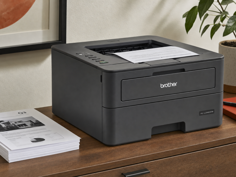 Brother HL-L2460DW wireless monochrome laser printer on a desk with printed documents for home office scale.